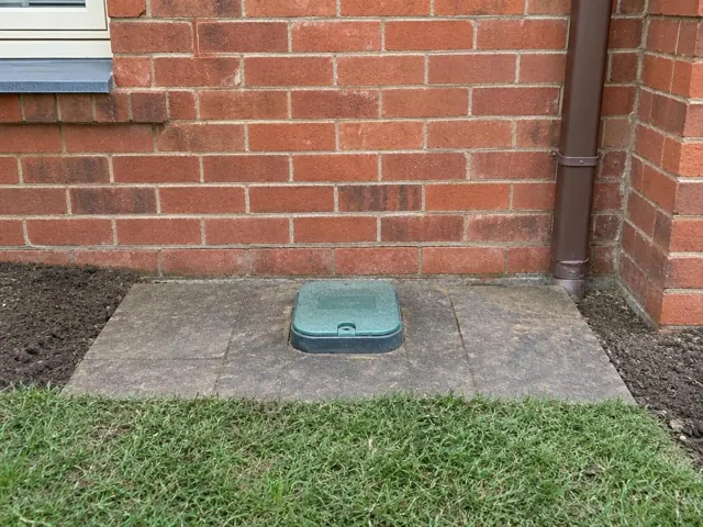 Capped sewer inspection opening set in paved patio beside a brick wall in Eastwood